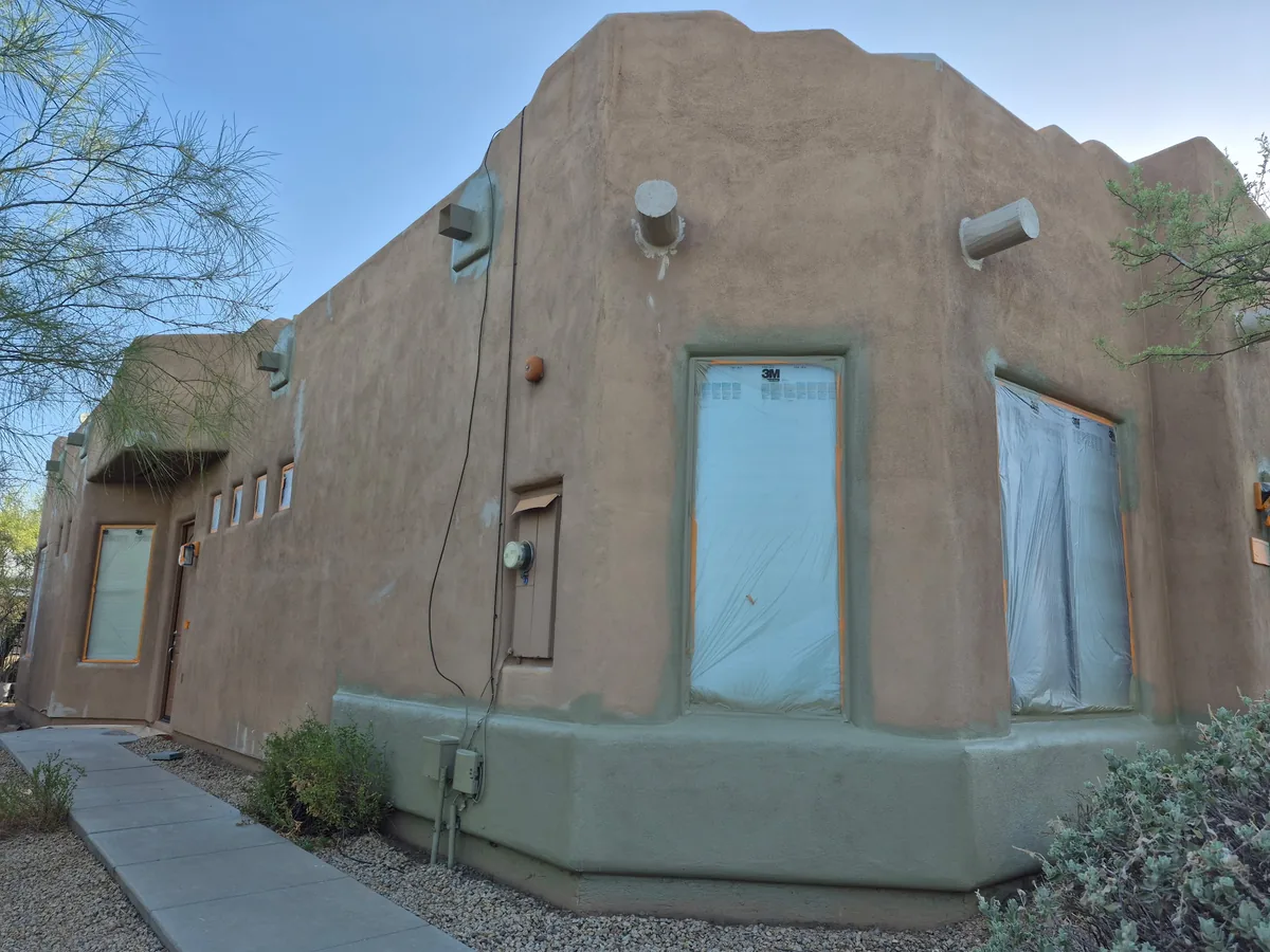 Stucco home exterior with windows and doors masked off in plastic before painting