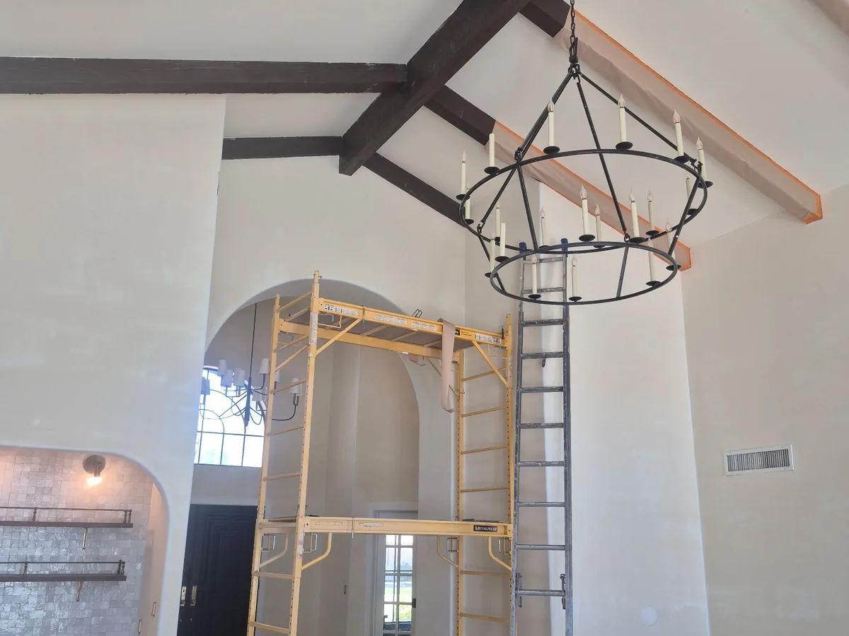 Scaffolding set up inside a two story great room with wood ceiling beams and an arched window