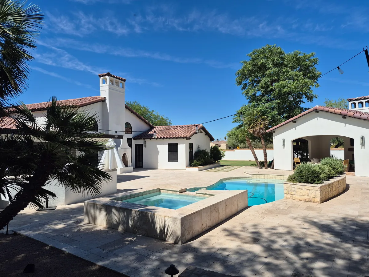 Stucco home with a tile roof and chimney overlooking a backyard pool and spa