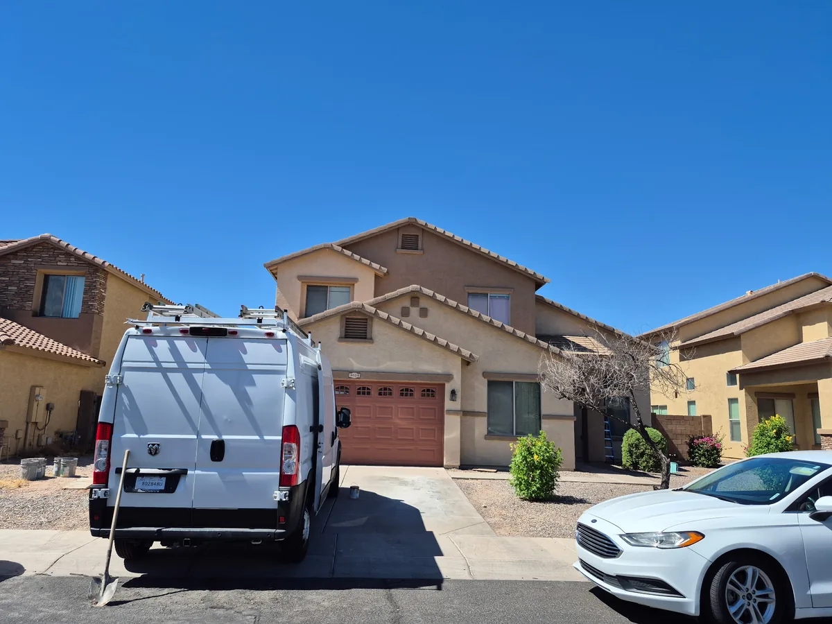 Tan stucco two story home with a red garage door and our work van parked out front