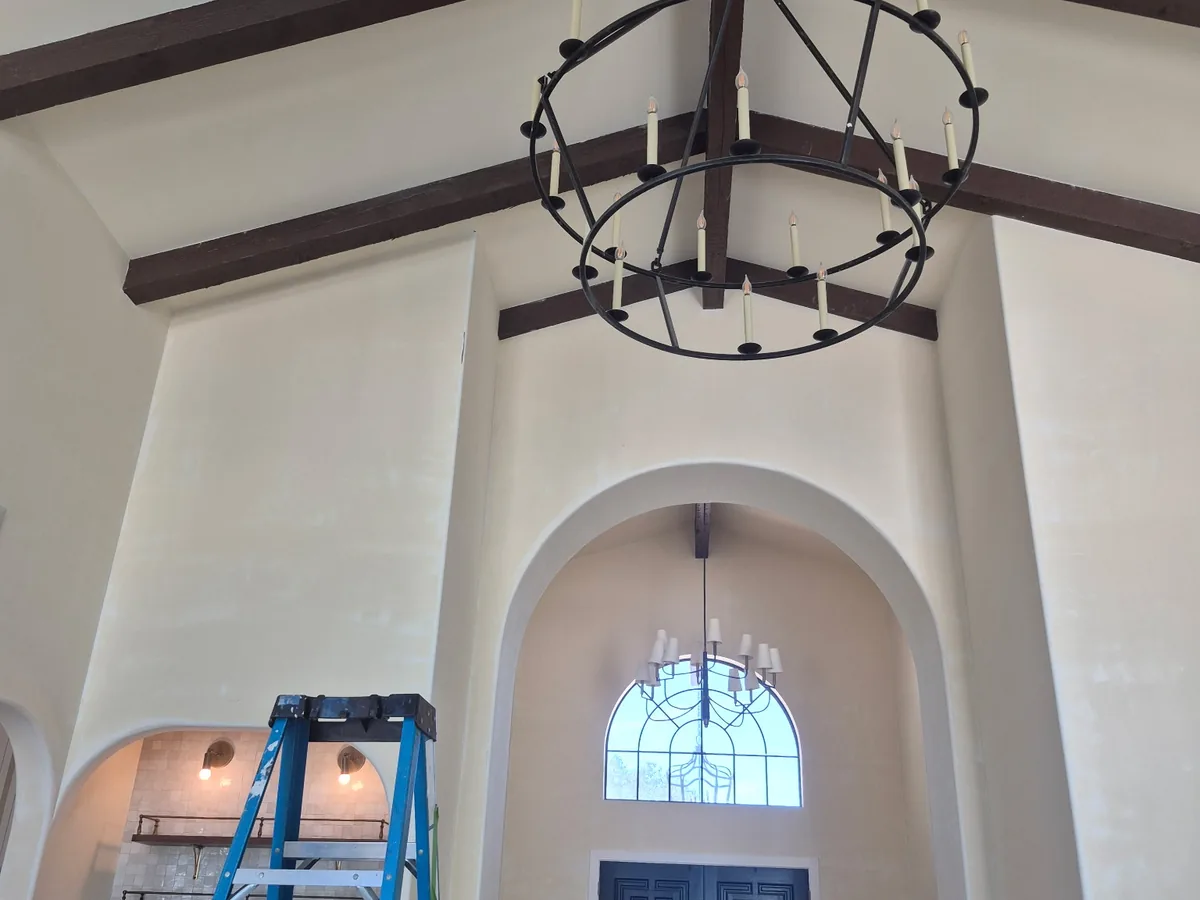 Vaulted great room with exposed wood beams, an iron chandelier and a ladder
